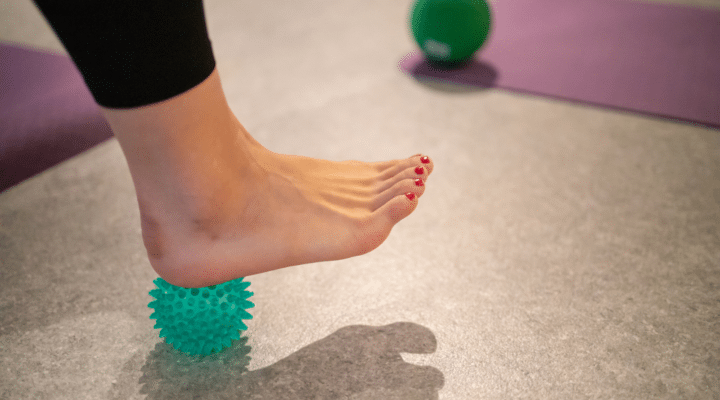Young woman massaging her heel with ball to alleviate foot pain