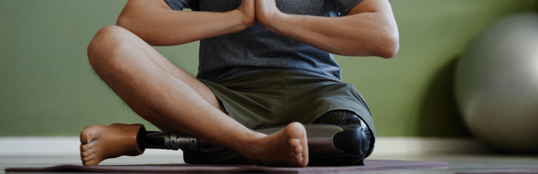 Adult man with prosthetic leg enjoying yoga workout indoors and meditating